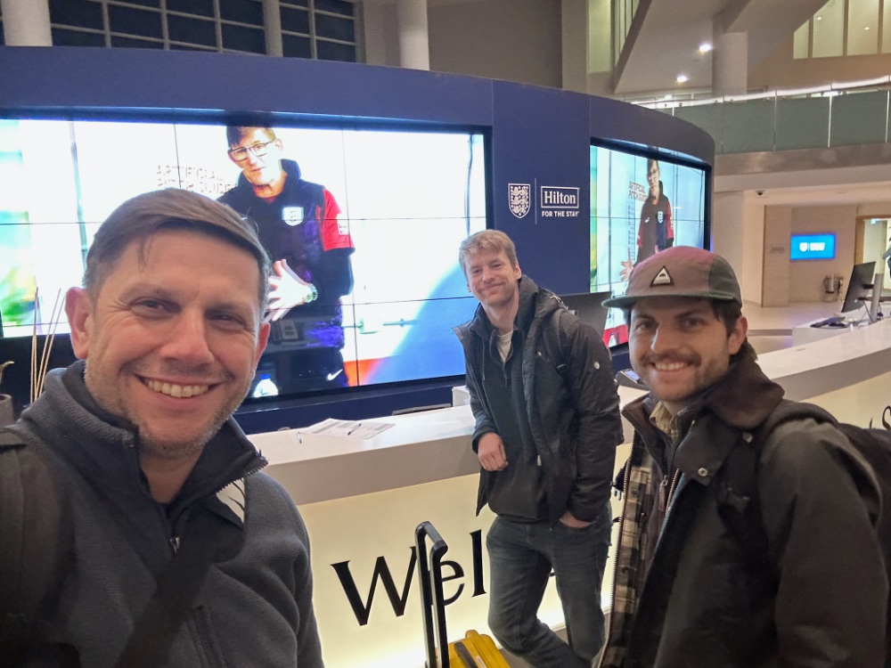 Three crew members selfie in front of a large video display wall