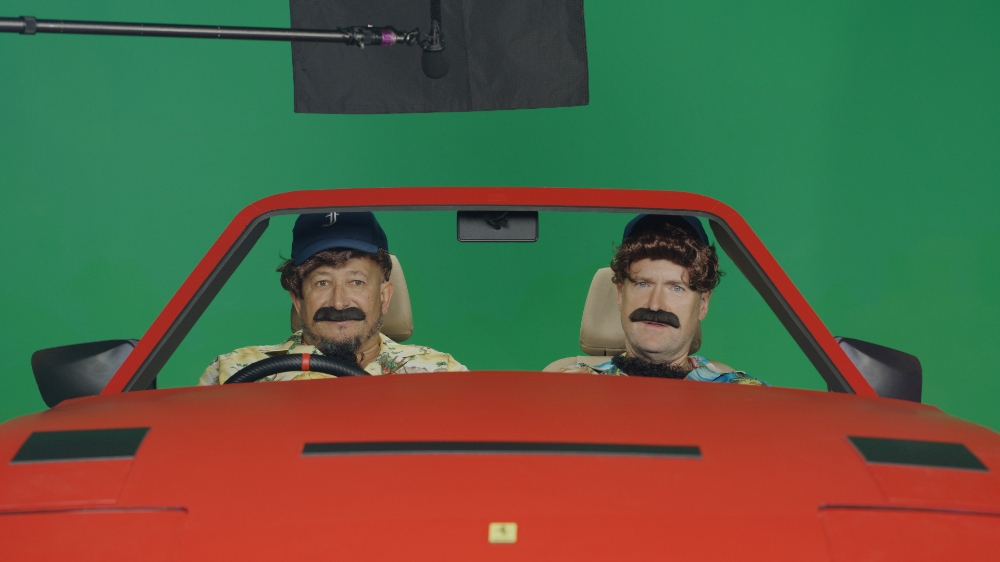 Two men in disguise costumes inside red Ferrari on green screen