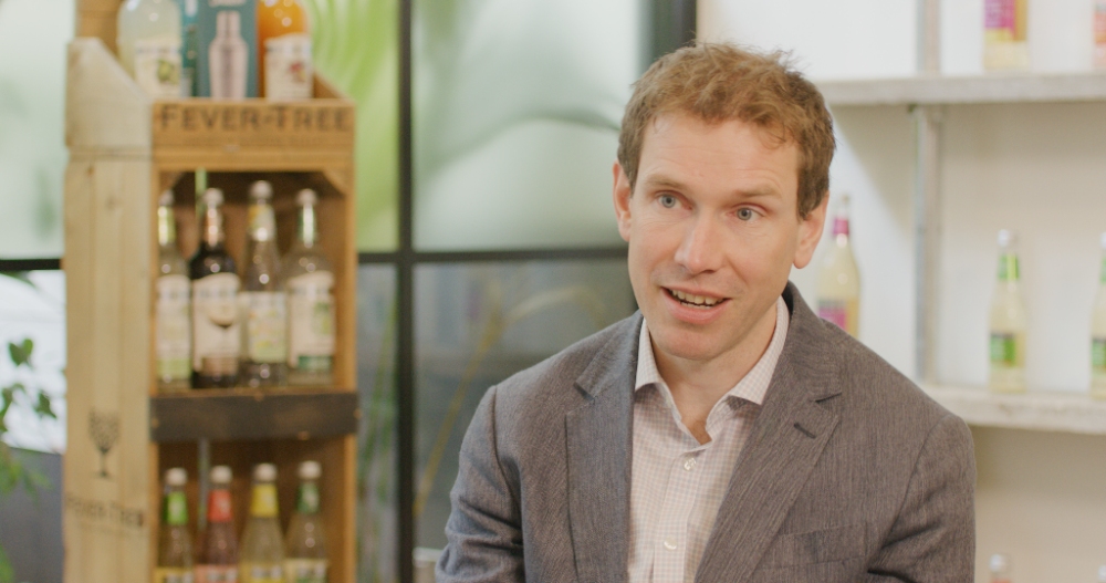 Man in blazer speaking on camera near Fever-Tree product display