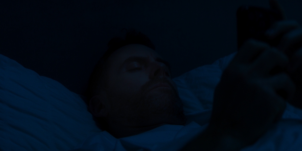 Man on Phone at Night Man lying in dark bedroom scrolling on a phone