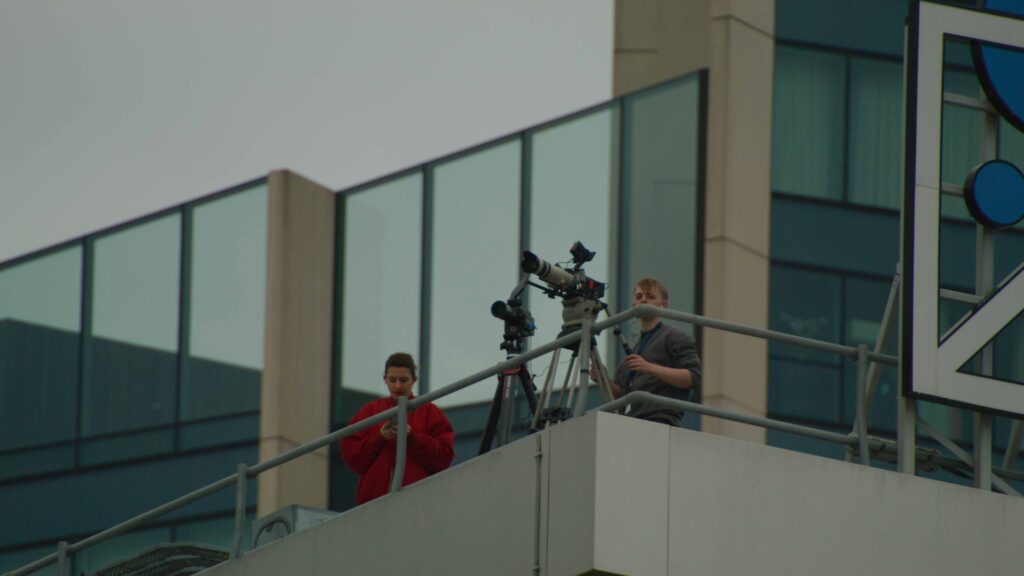 Rooftop Film Crew Camera crew filming from a rooftop balcony with tripod