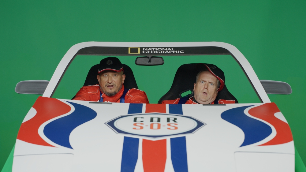 Two men in Car SOS branded car on green screen set
