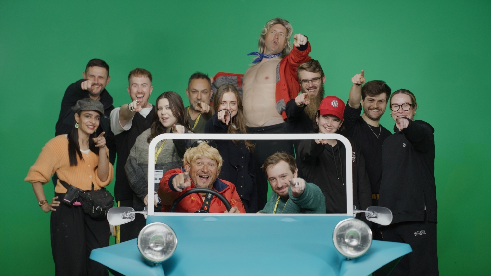 Car SOS cast and crew posing around blue prop car on green screen