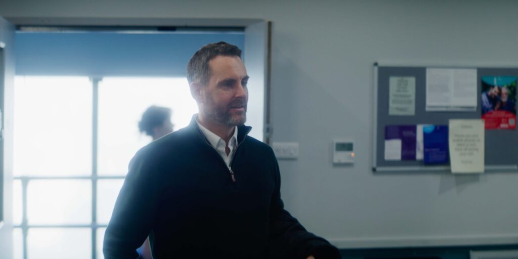 Man in black jumper standing in a bright office or classroom