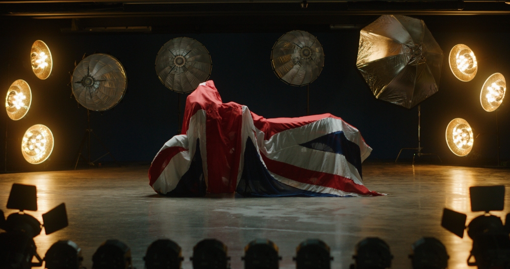 Union Jack Car Reveal Car draped in Union Jack flag on dramatic studio stage