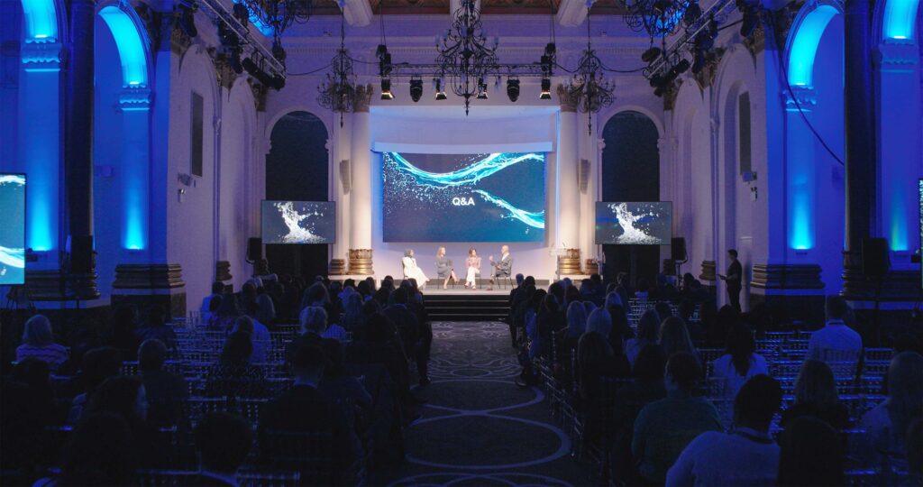 Audience watching a large LED screen at a blue-lit conference event