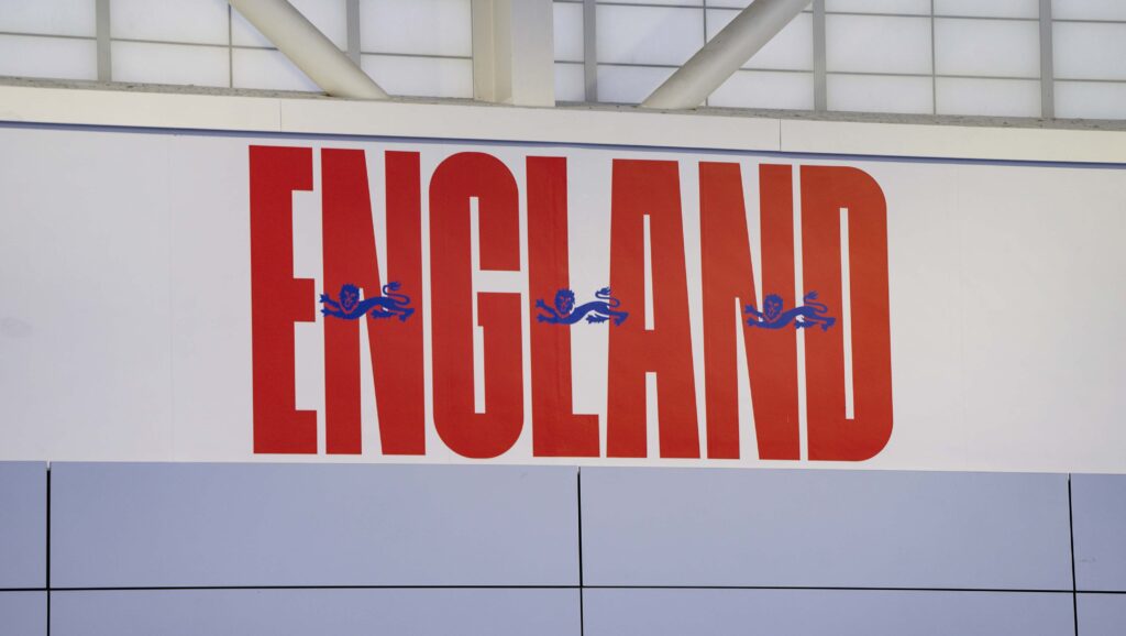 Bold red England sign with Three Lions badge on white wall