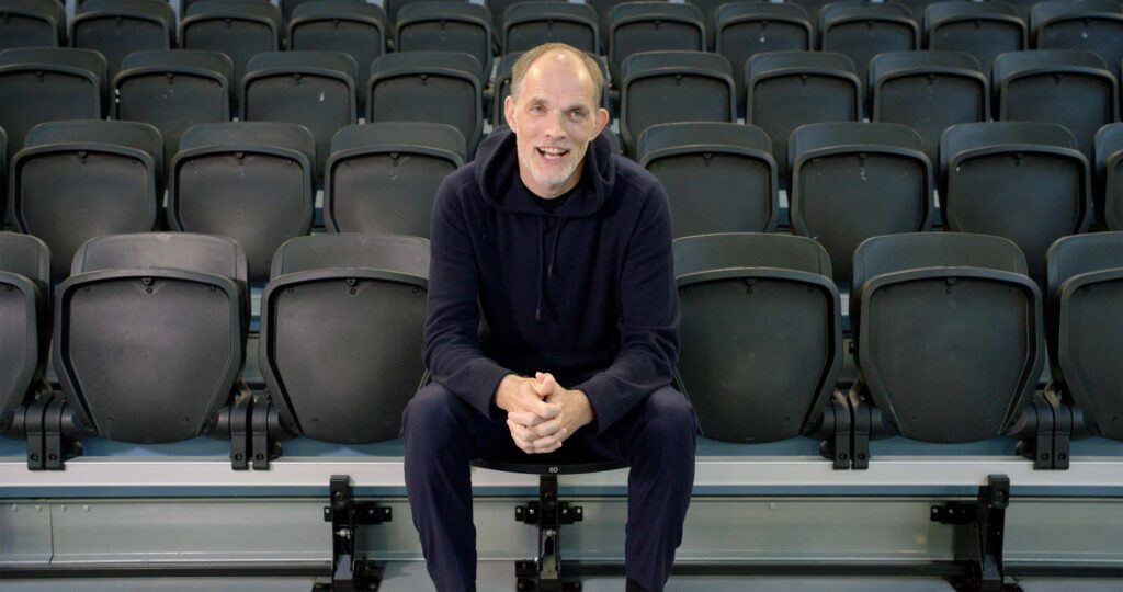 Man sitting alone in empty stadium seating, smiling at camera