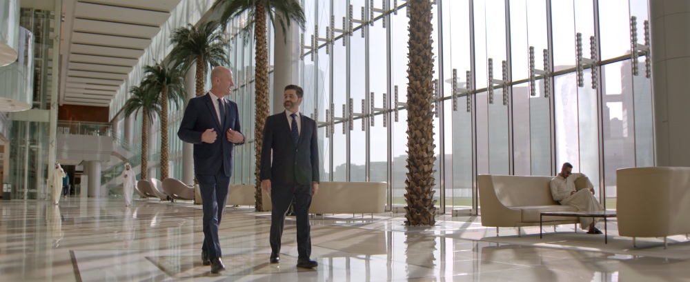 TEUR Corporate Lobby Walk Two men in suits walking through a modern glass lobby with palms