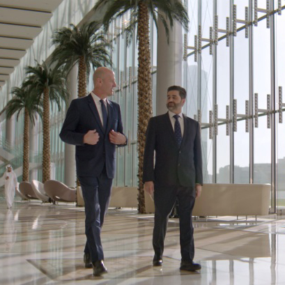 Two businessmen walking through modern glass lobby with palm trees