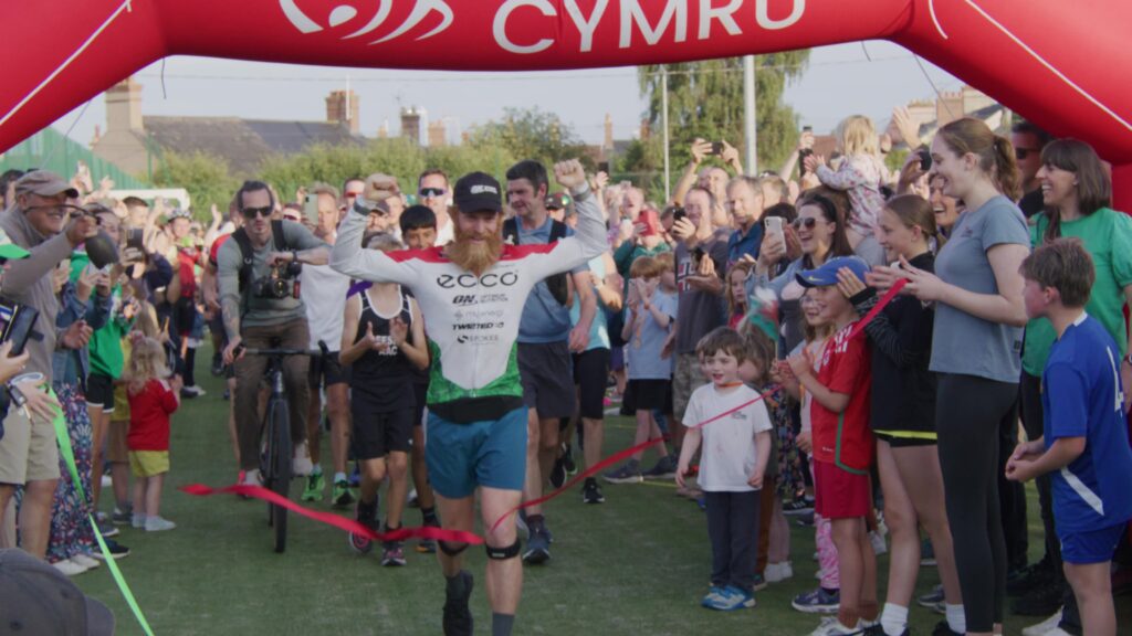 Runner crossing finish line at Cymru event with crowd cheering