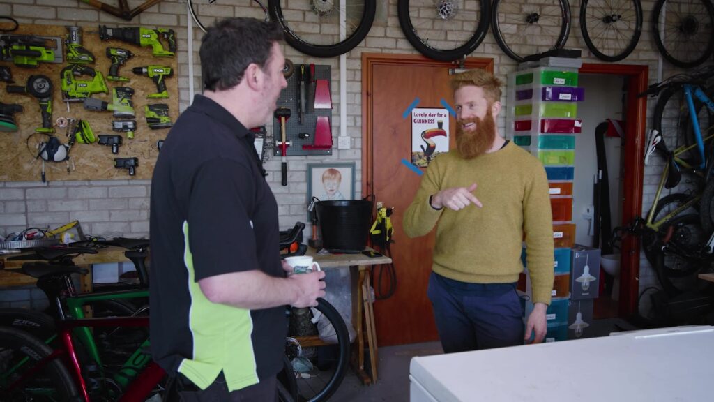 Two men talking in a bike repair workshop with tools