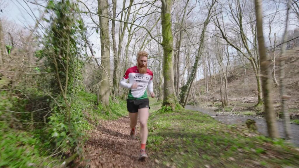 Runner in red and white kit trail running through woodland