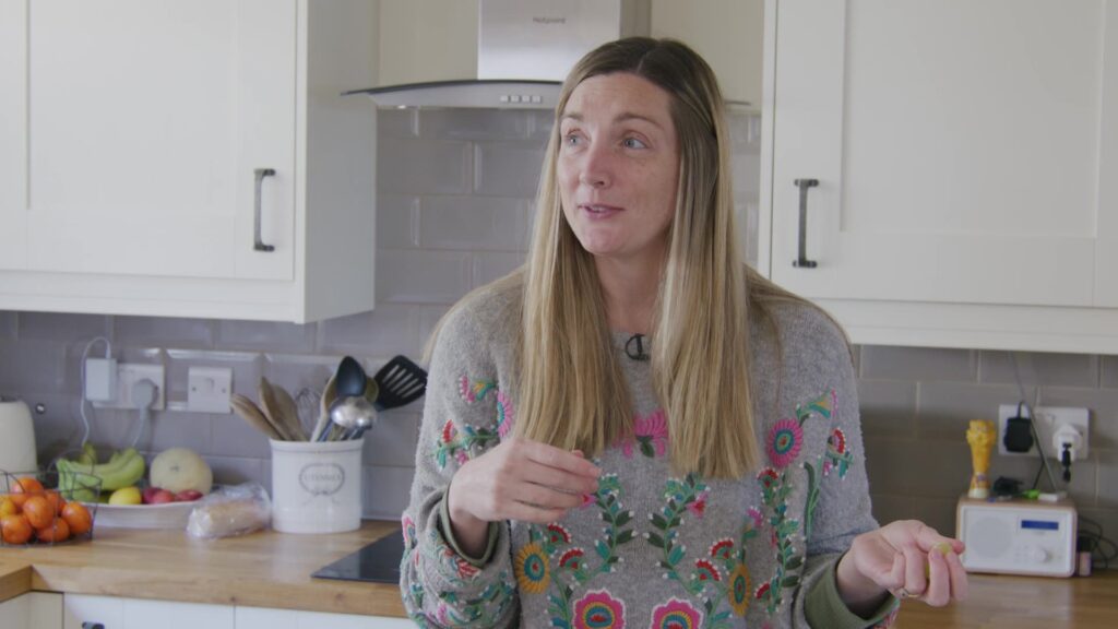 Woman in floral apron talking in a home kitchen