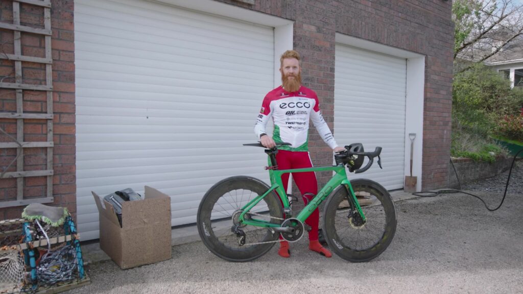 Red-bearded cyclist in ECCO kit standing with green road bike
