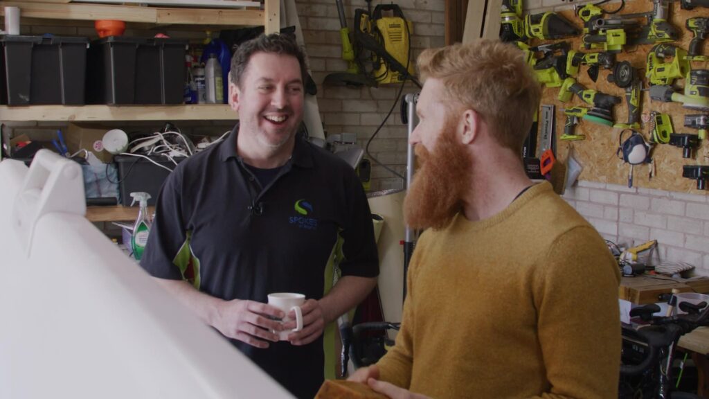 Two men laughing and chatting in a workshop over coffee