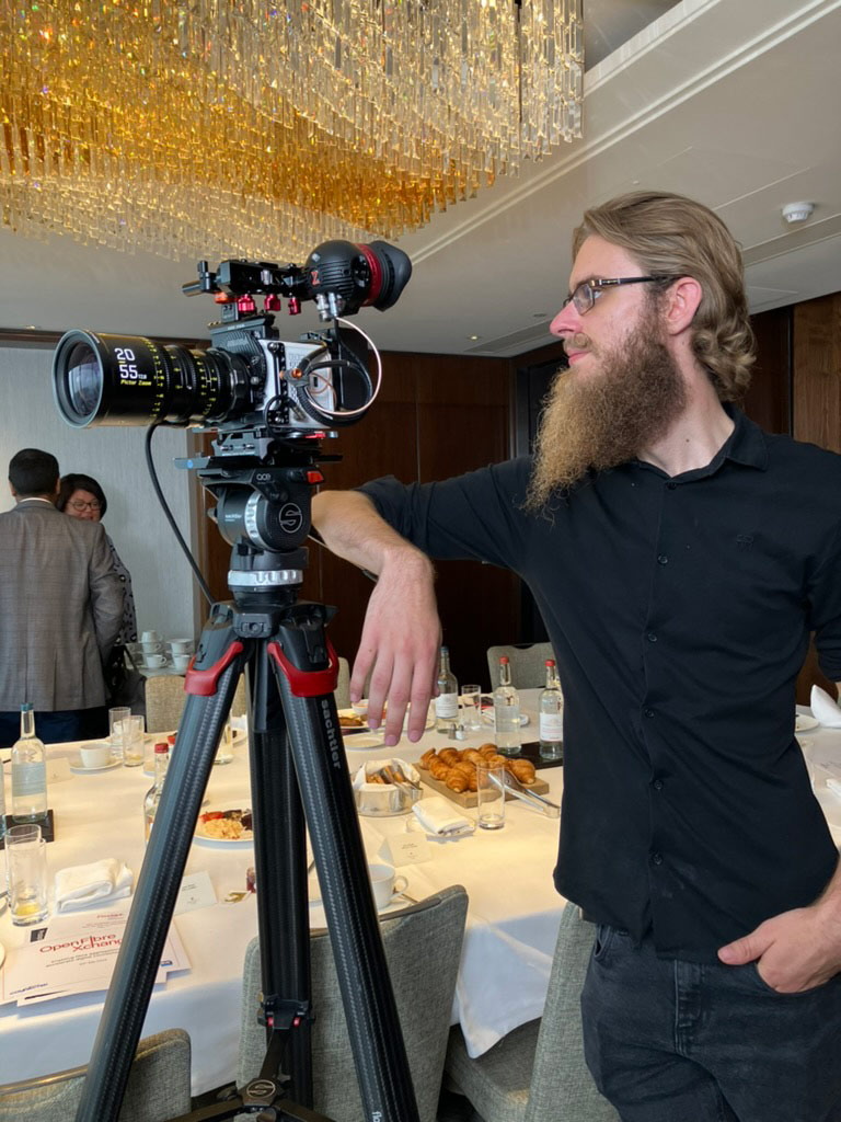 Videographer on Set Bearded man leaning on a camera on tripod in restaurant