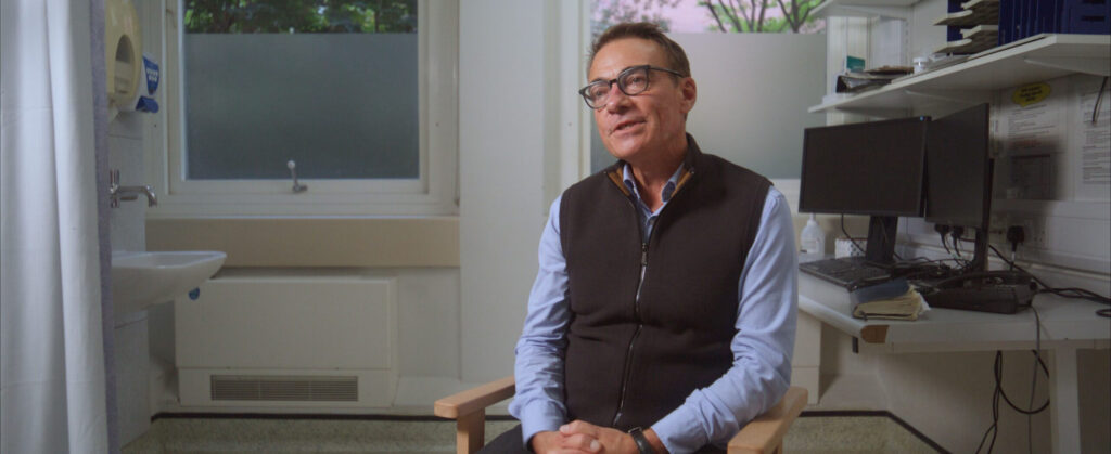 Man sitting in a chair in a clinical room, speaking to camera