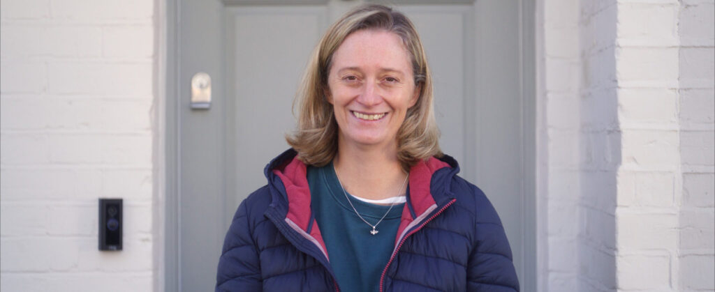 Smiling woman in blue jacket standing outside a white building