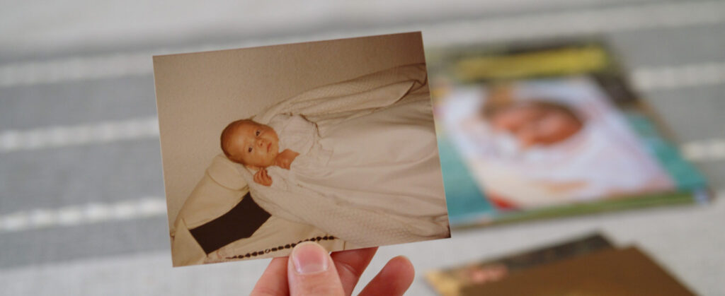Hand holding an old photo of a baby in white clothing